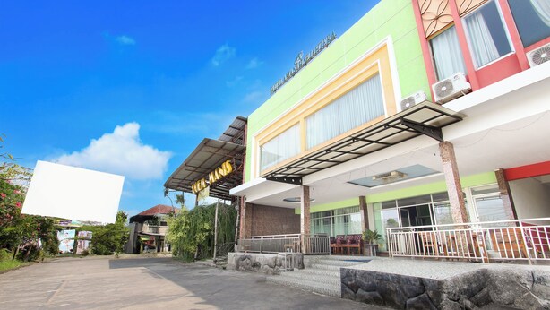 A hotel with a green and white facade, multiple air conditioning units, a covered entrance, and a large empty parking lot. - Hotel O Jalan Slamet Riyadi Near Bandara Adi Soemarmo Formerly Amanah Sejahtera (Ngemplak)