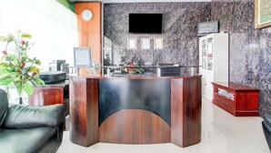 A reception desk with a clock, framed certificates, a flat-screen TV, and a refrigerator. - Hotel O Jalan Slamet Riyadi Near Bandara Adi Soemarmo Formerly Amanah Sejahtera (Ngemplak)