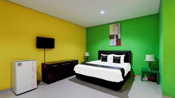 Un dormitorio con cama, televisión, refrigerador y mesita de noche con lámpara.