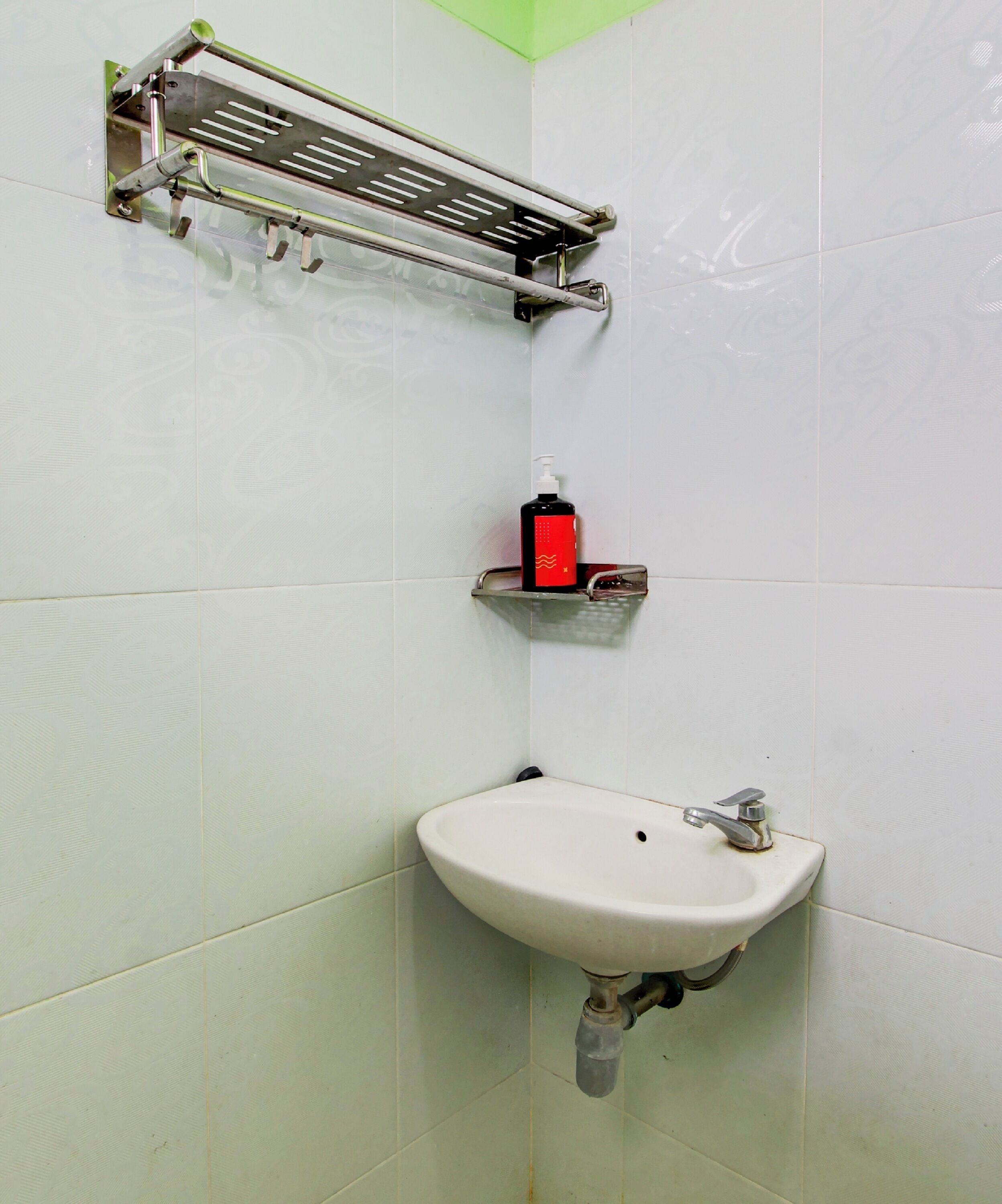 Un baño con lavamanos blanco, dispensador de jabón y toallero metálico.