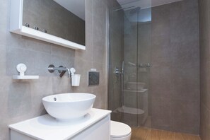 Ein modernes Badezimmer mit einem weißen Waschbecken, einer Duschkabine aus Glas und einer Toilette.