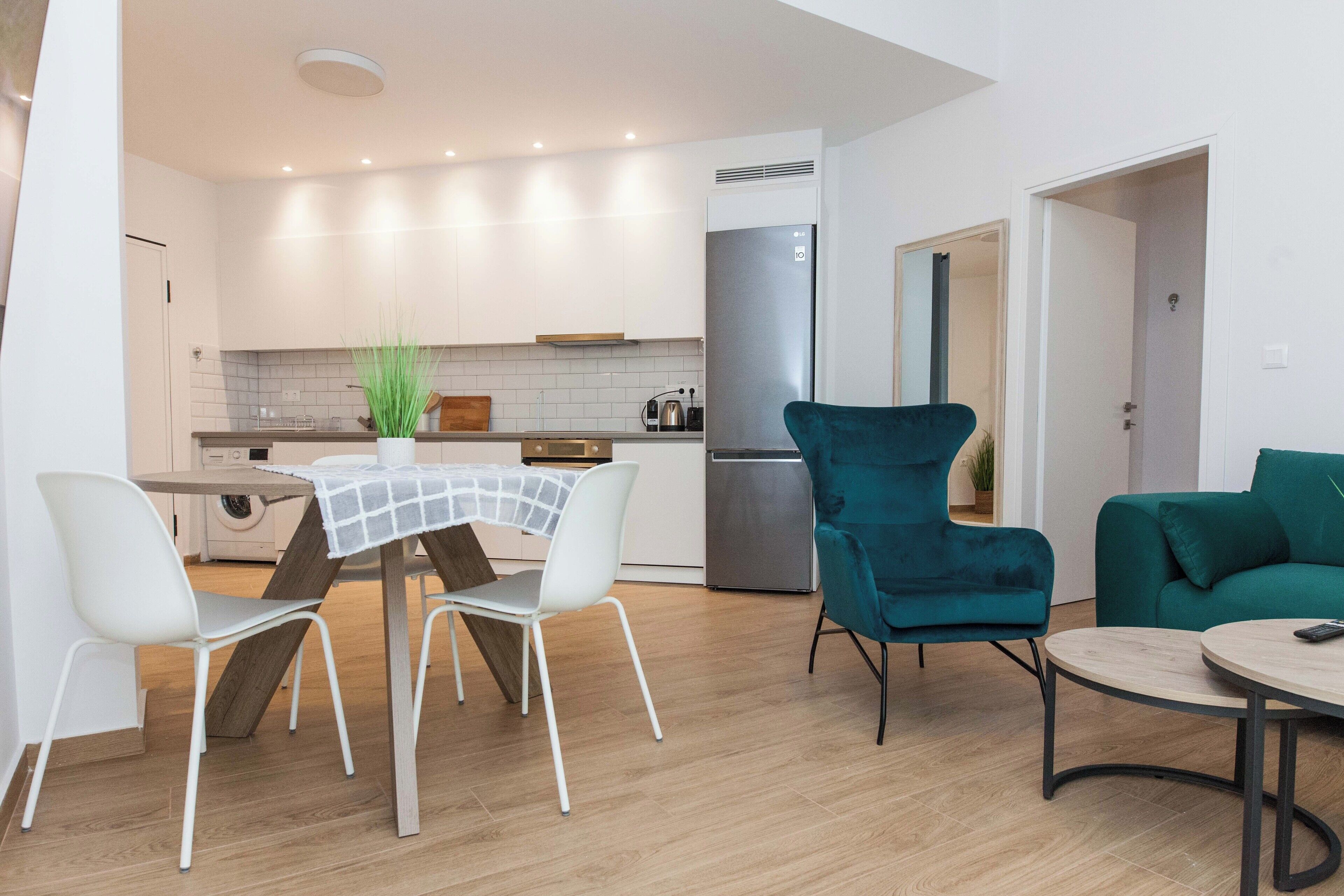 Une cuisine moderne avec des meubles blancs, un réfrigérateur en acier inoxydable et un coin repas comprenant une table et des chaises.