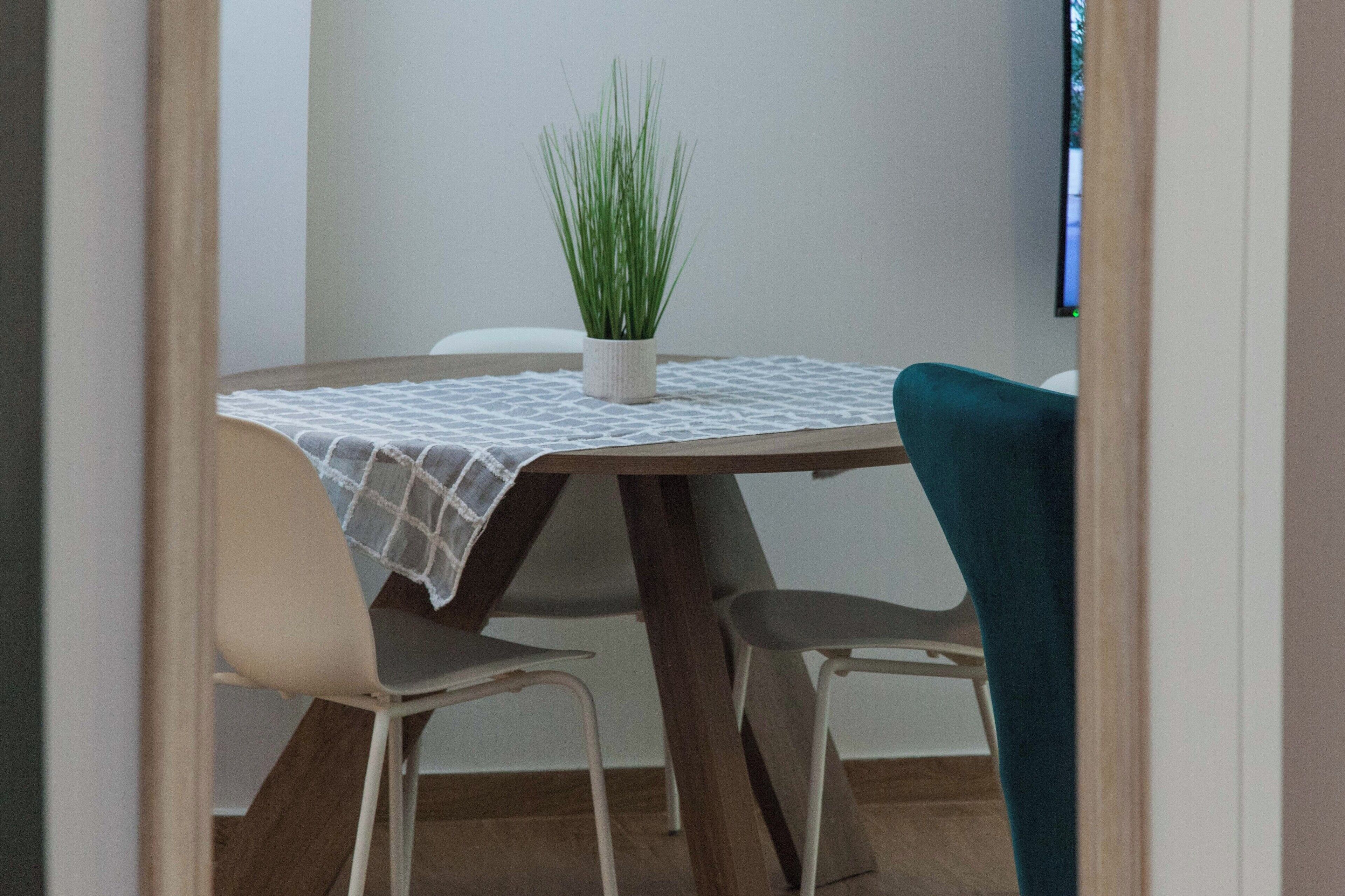 A dining area with a round table, two chairs, a small potted plant, and a white tablecloth.