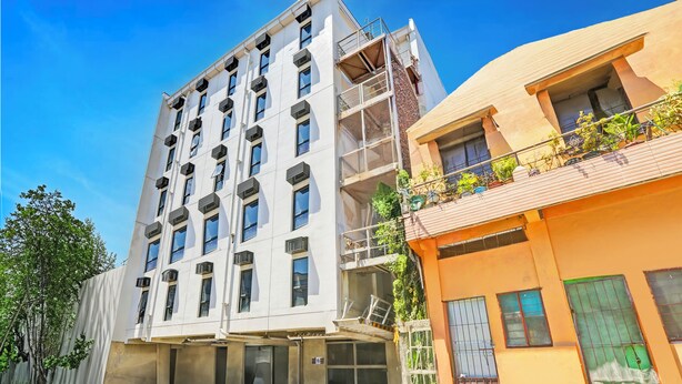 A multi-story building with a modern architectural design, featuring a flat facade, large windows, and a balcony with potted plants. - Spot On Classy Bunkbeds Near Makati Manila Formerly MYTOWN Madrid (Taguig)