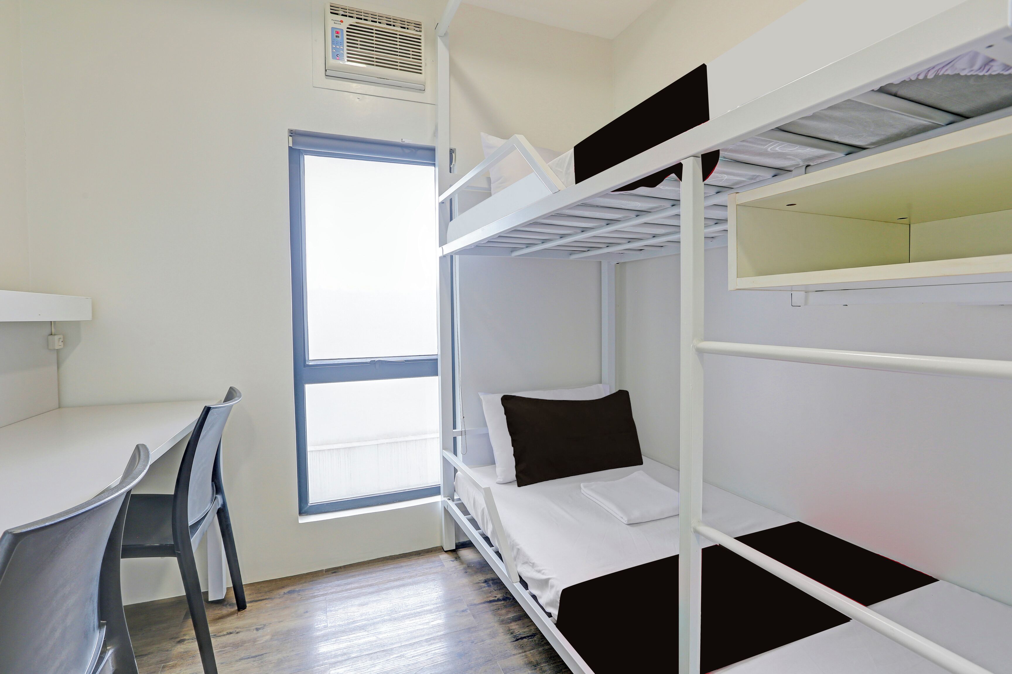 Habitación con literas, escritorio, silla, ventana y pared blanca.