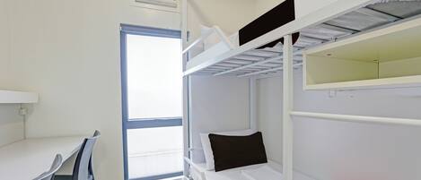 Habitación con literas, escritorio, silla, ventana y pared blanca.