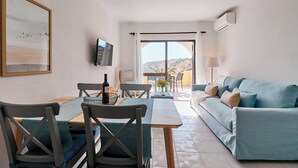 En moderne stue med sofa, spisebord, stole og et tv ophængt på væggen.