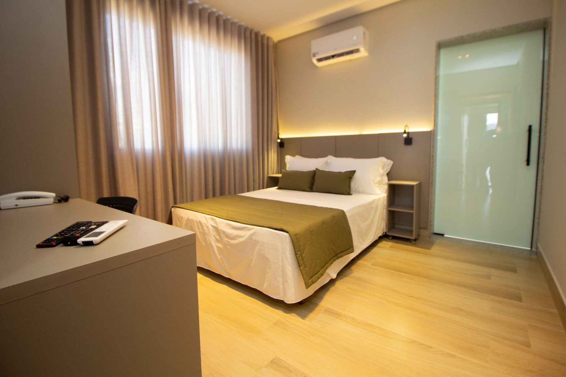 A hotel room with a bed, bedside table, and a desk with a phone and remote control.