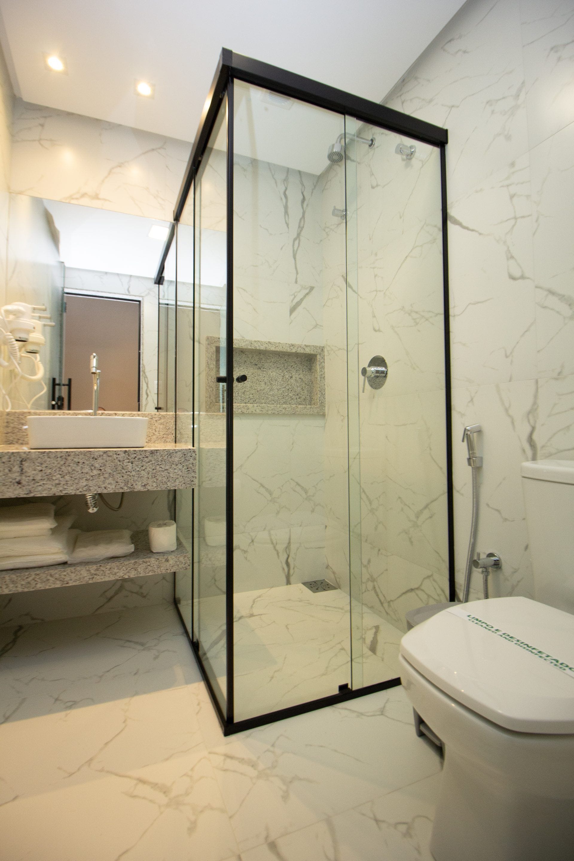 A modern bathroom with a glass-enclosed shower, a marble-tiled floor, and a white toilet.