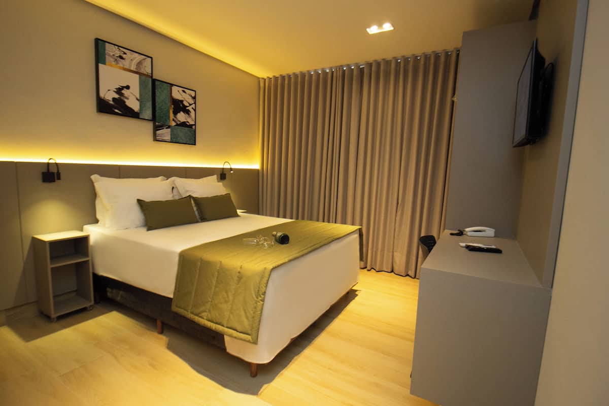 A modern hotel room with a neatly made bed, a bedside table, a flat-screen TV, and artwork on the wall.