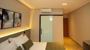 Habitación de hotel con cama, mesita de noche, aire acondicionado instalado en la pared y puerta que da a un pasillo.