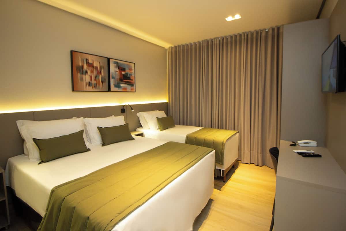 A hotel room with two beds, a desk, a television, and artwork on the wall.