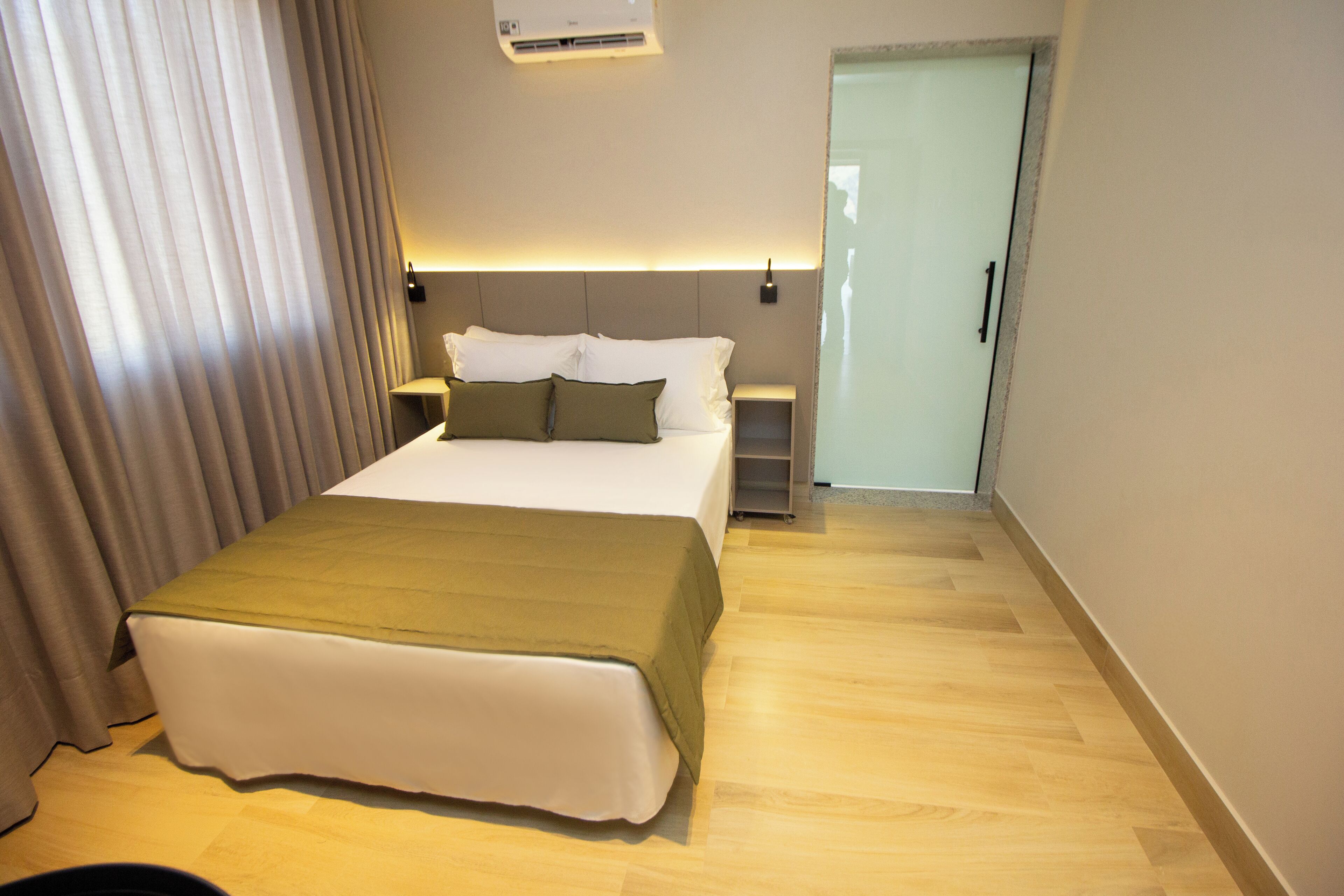 A hotel room with a bed, bedside tables, and a door leading to another room.