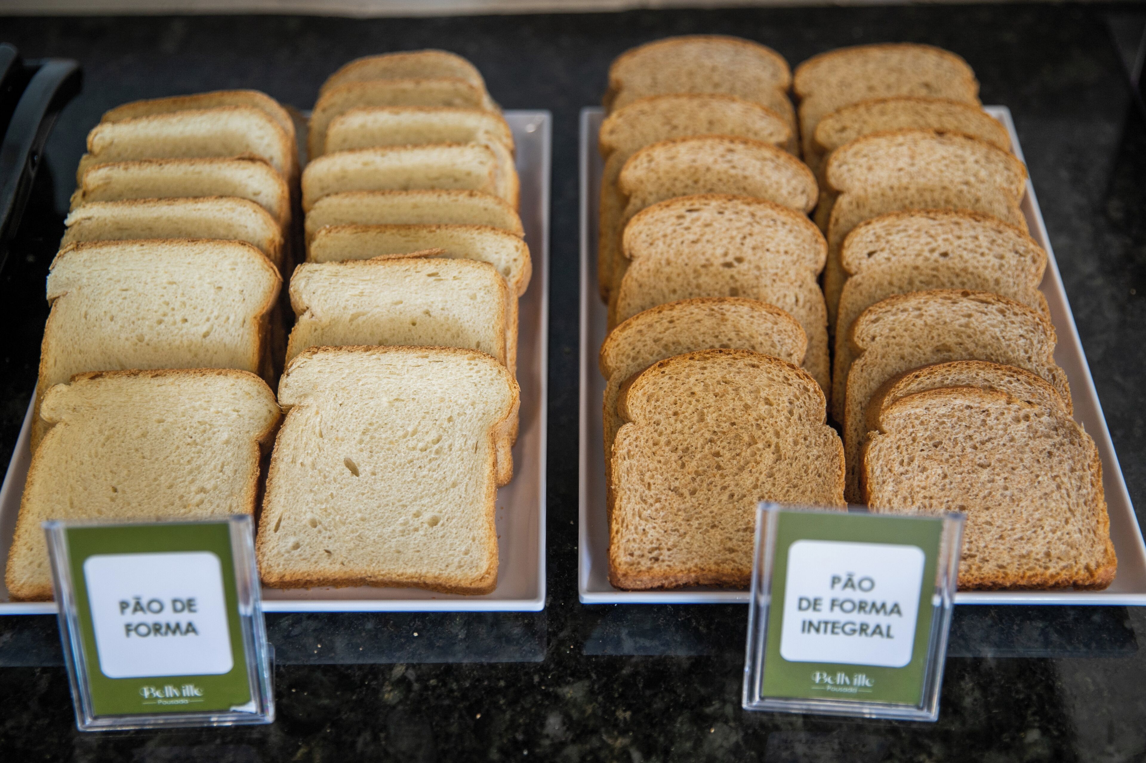Two trays of bread labeled "Pão de Forma" and "Pão de Forma Integral" on a counter.