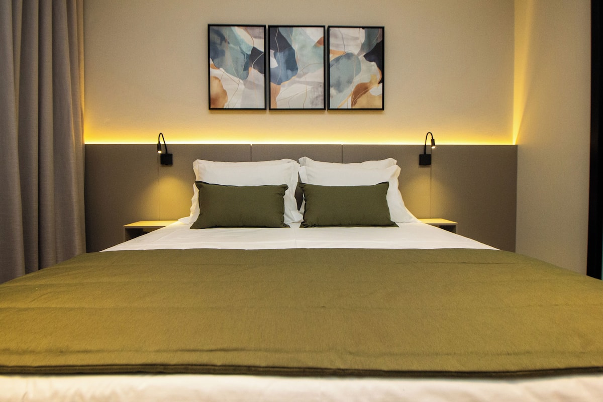A hotel room with a large bed, two bedside tables, and abstract wall art.