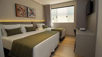 A hotel room with two beds, a desk, a chair, a TV, and artwork on the wall.