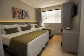 A hotel room with two beds, a desk, a chair, a TV, and artwork on the wall. - Bellville Pousada (Capitólio)