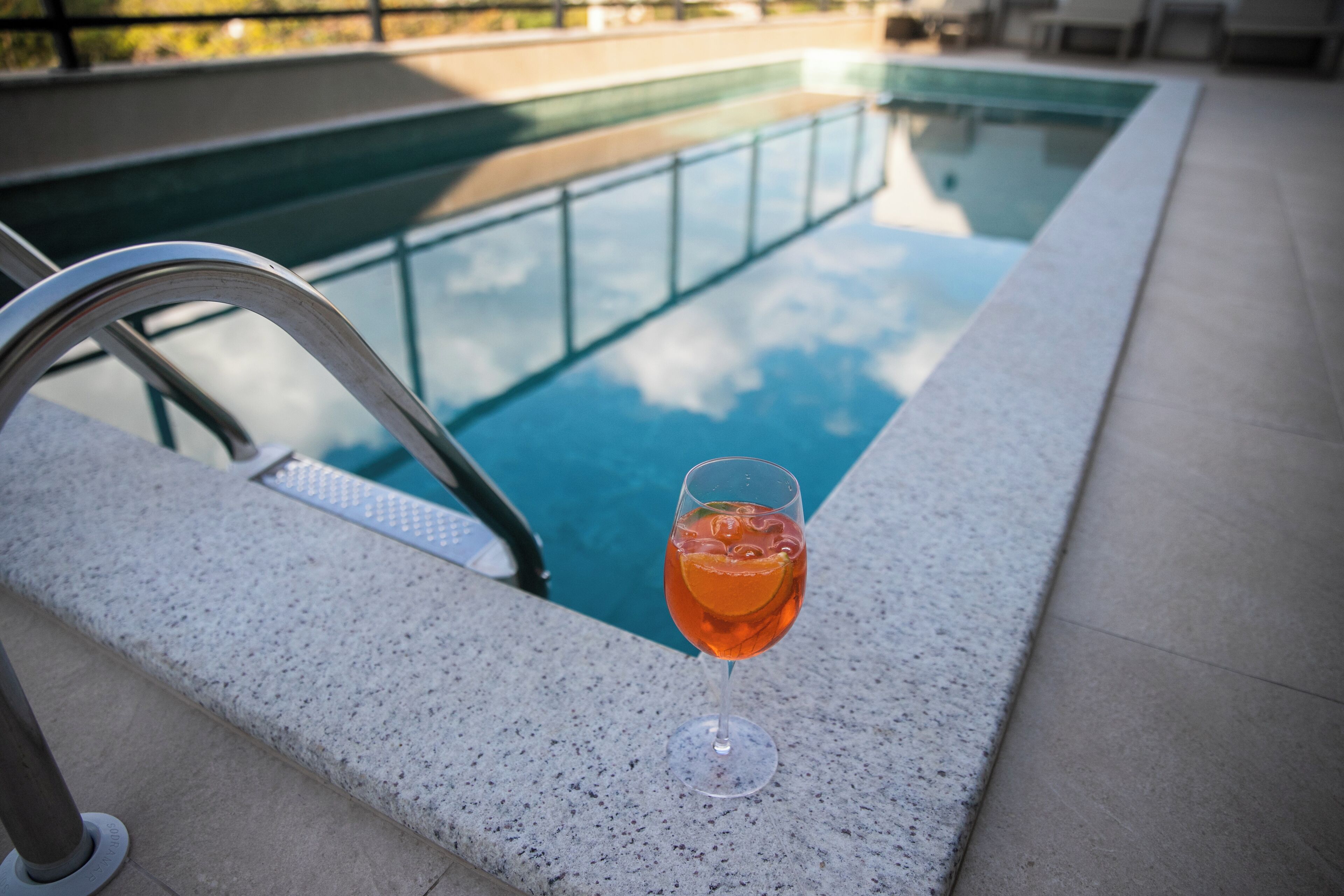 A glass of orange drink on a poolside ledge with a clear pool in the background.