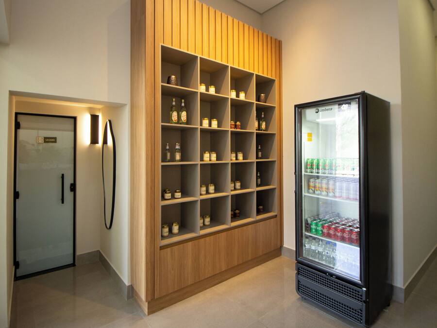 A modern hotel room with a wooden shelving unit filled with jars and a minibar refrigerator stocked with beverages.