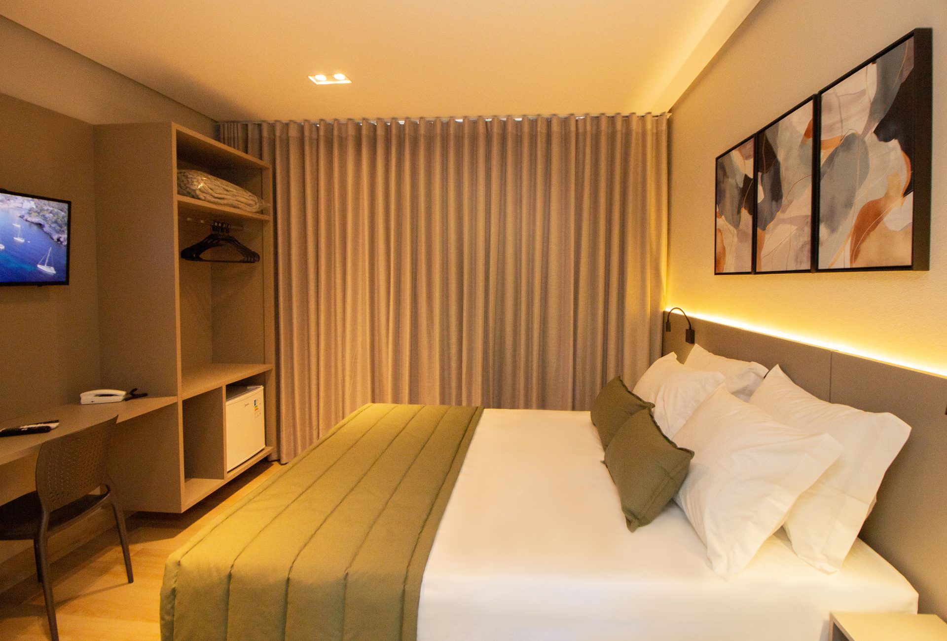 A hotel room with a bed, a desk, a television, and a painting on the wall.