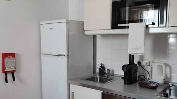 Una cocina compacta con armarios blancos, un refrigerador de acero inoxidable, un microondas y una cafetera.