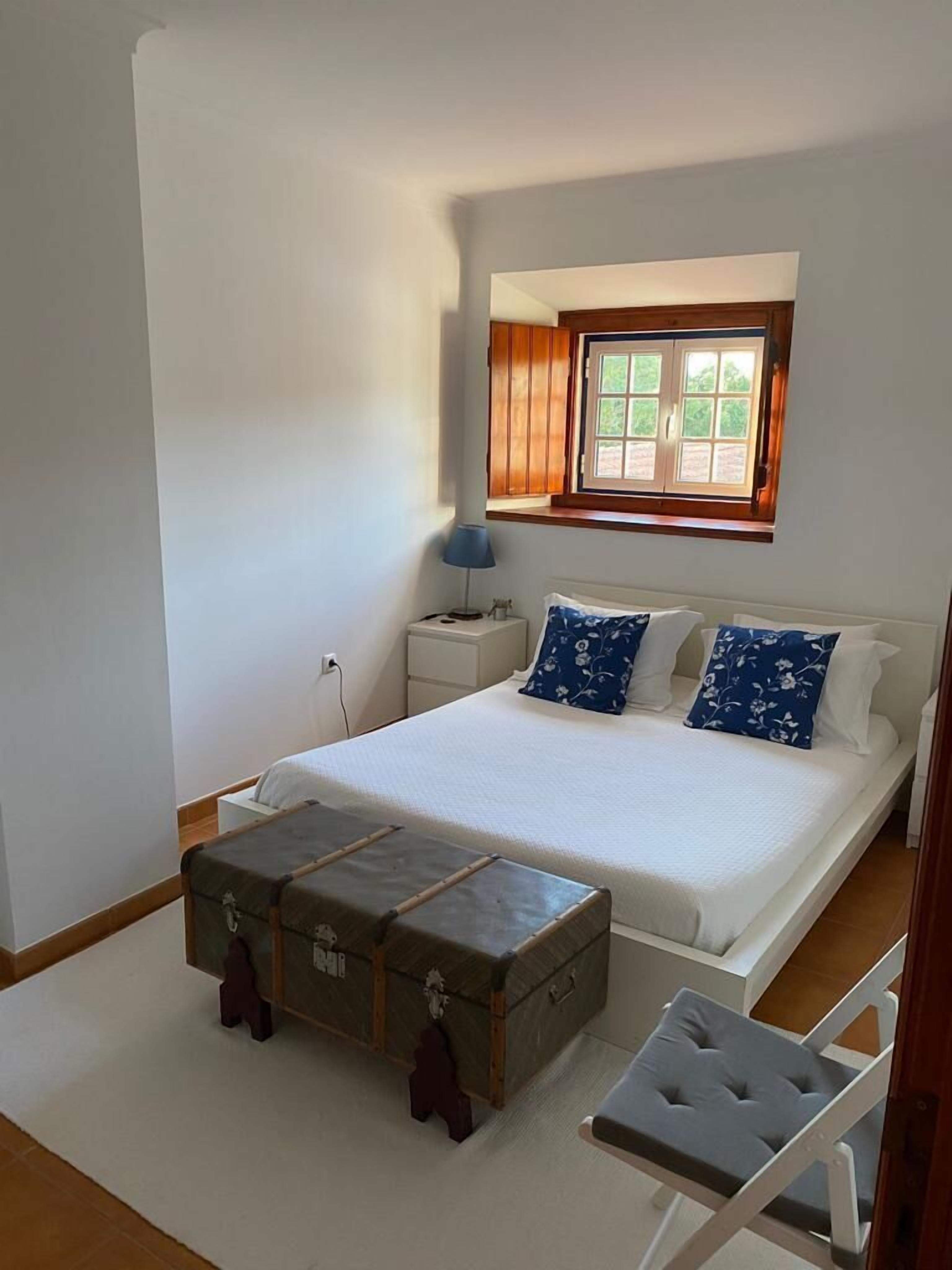 Un dormitorio con cama, mesita de noche, lámpara, ventana y cómoda.
