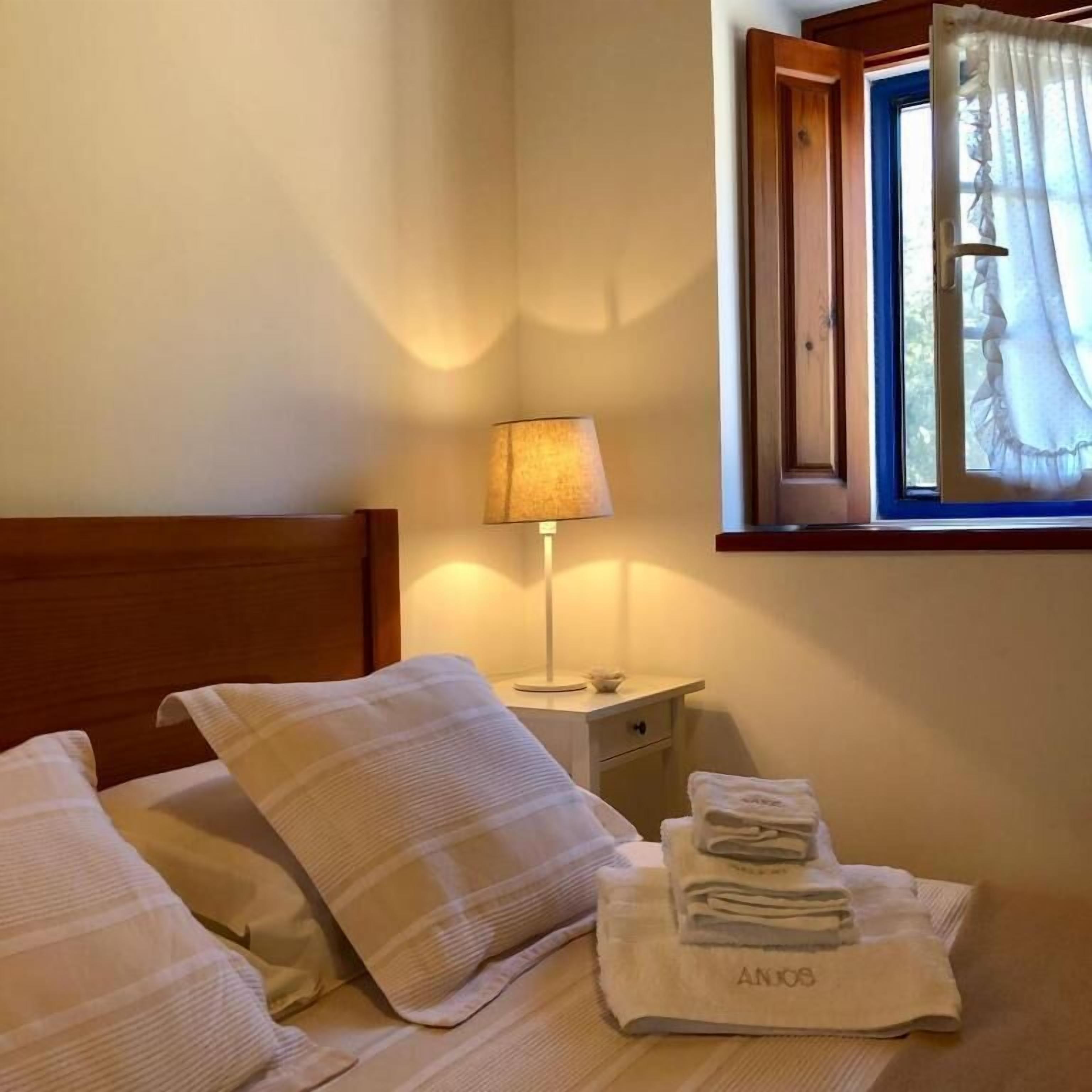 Cama bem arrumada com travesseiro e toalha dobrada em cabeceira de madeira.