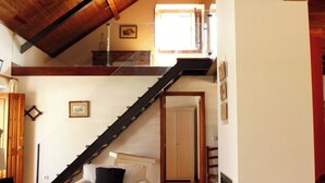 A spacious loft with a high ceiling, a wooden staircase, a sofa, and a fireplace. - Quinta dos Anjos (Santarém)