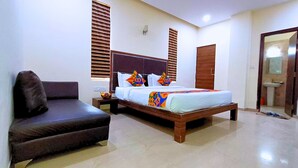A bedroom with a bed, a nightstand, a chair, a wardrobe, and a bathroom visible through an open door. - Maharana Palace by Asapian Hotels (Amer)