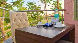 A balcony with a table set for two, a chair, and a view of greenery and buildings. - Maharana Palace by Asapian Hotels (Amer)