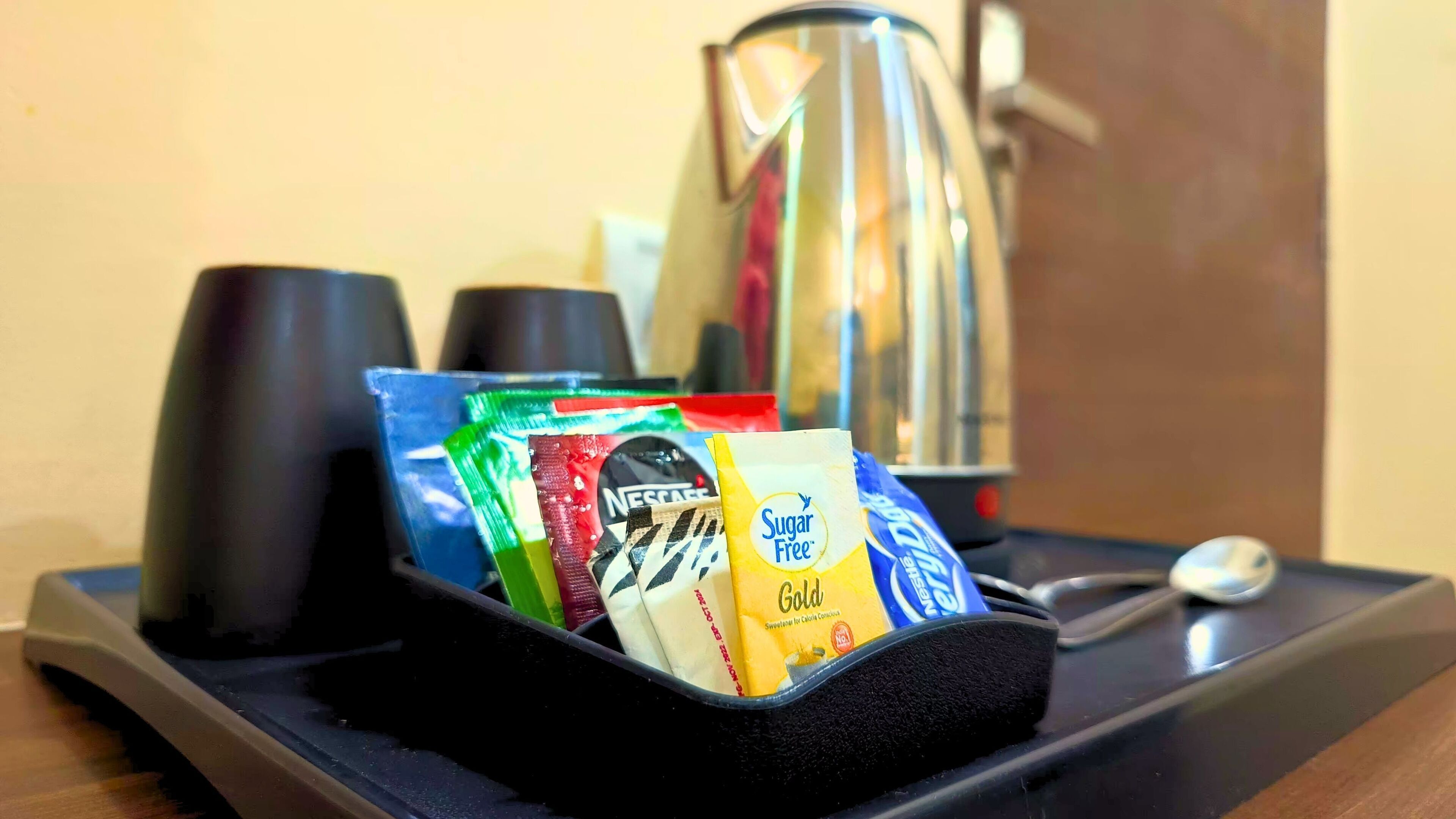 Un plateau avec une cafetière, des tasses et des sachets de sucre.