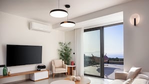 A modern living room with a flat-screen TV, a sofa, a coffee table, and a large window with a view.