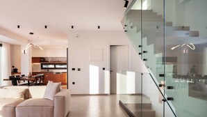 A modern living room with a glass staircase, a dining area, and a kitchen in the background.