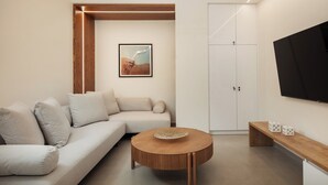 A modern living room with a sofa, a round wooden coffee table, and a flat-screen TV mounted on the wall.