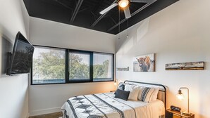 Ein modernes Schlafzimmer mit einem gro ßen Bett, einem Deckenventilator, einem an der Wand befestigten Fernseher und Kunstwerken an den Wänden.