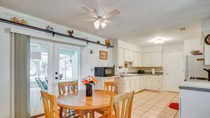 A modern kitchen with white cabinets, a microwave, and a gas stove. There is a dining area with a wooden table and chairs, and a ceiling fan above.