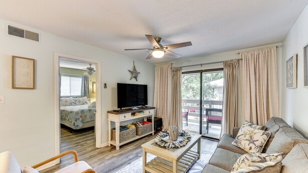A living room with a sofa, armchairs, a coffee table, a TV, and a ceiling fan. - 1/2 Mi to Folly Field Beach: Condo w/ 2 Pools (Hilton Head Island)