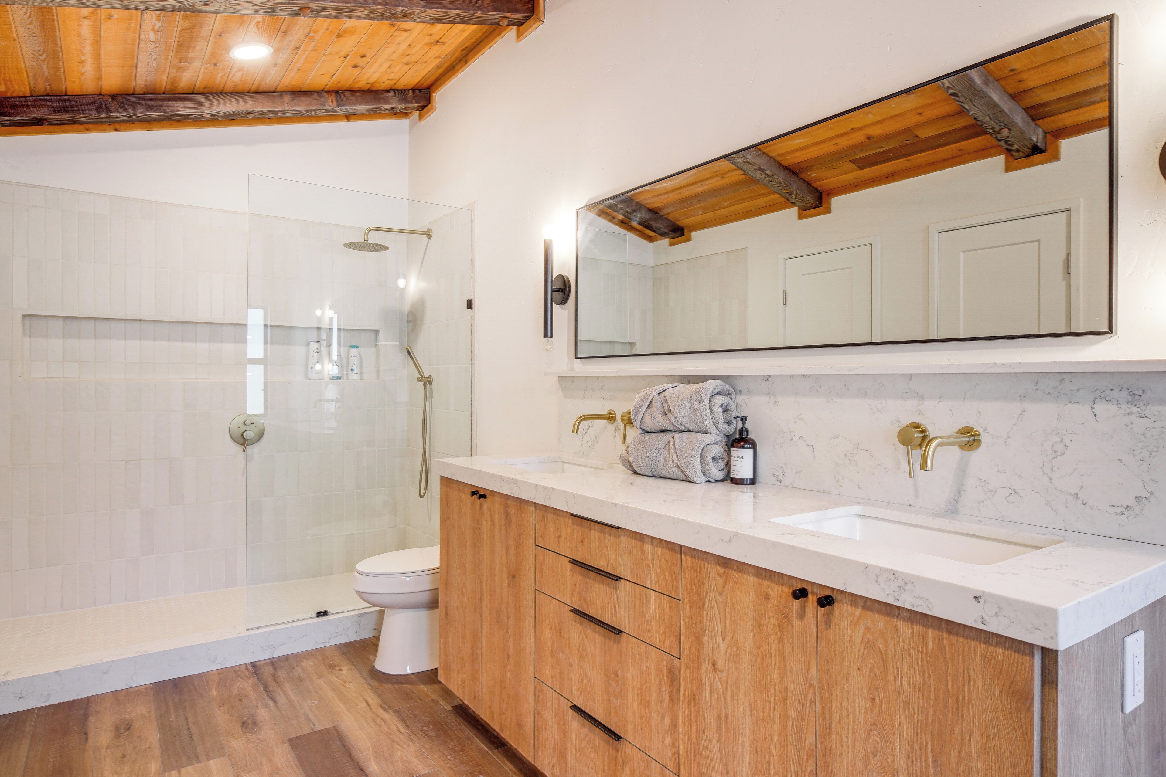 A bathroom with a glass-enclosed shower, a toilet, wooden cabinets, and a marble countertop.
