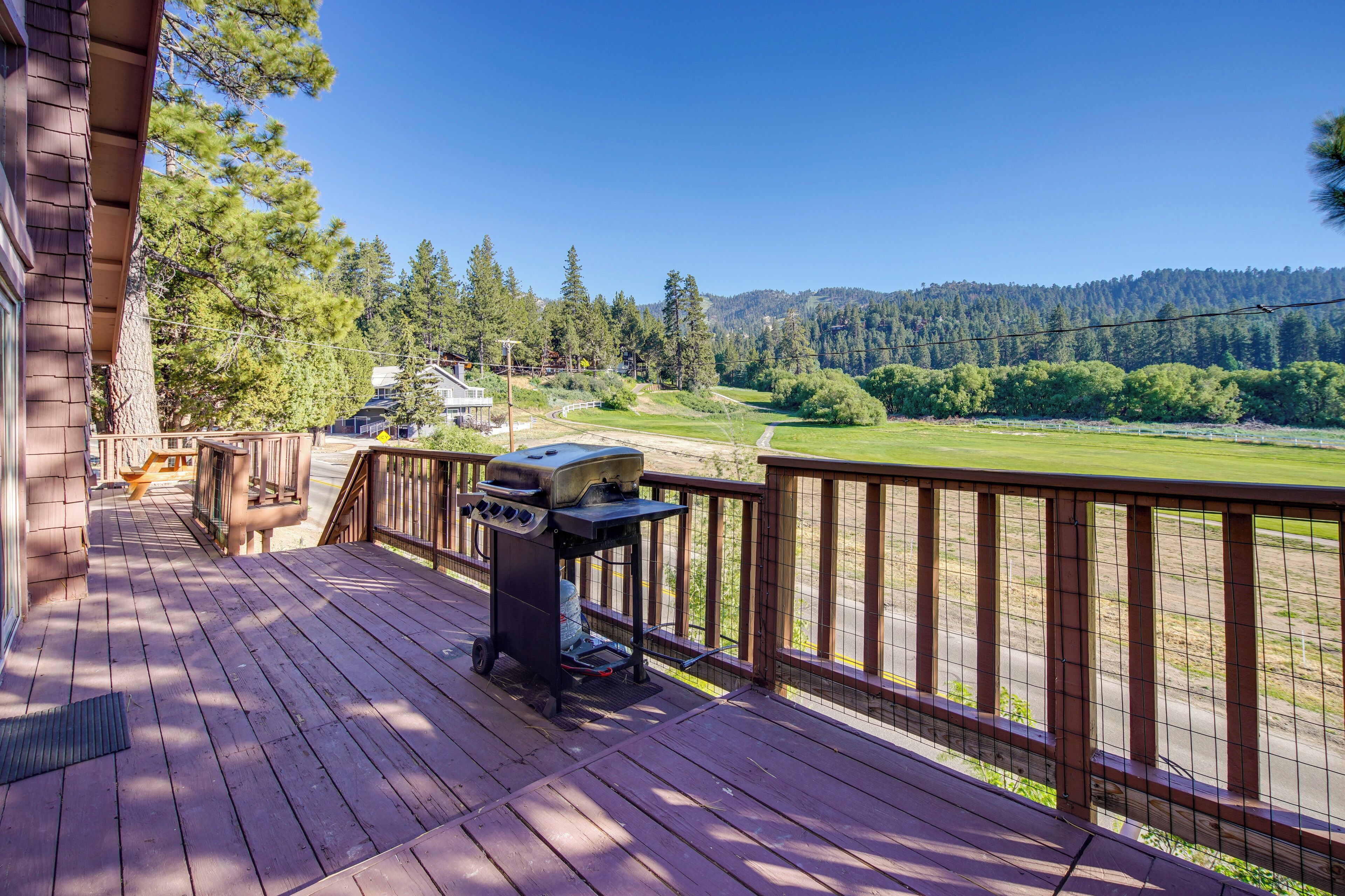 A wooden deck with a barbecue grill, overlooking a golf course and forested hills.
