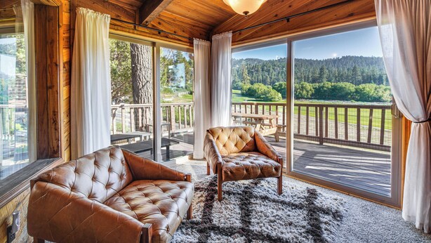Un intérieur en bois agrémenté de canapés en cuir, une grande fenêtre donnant sur une forêt et un balcon avec une balustrade.