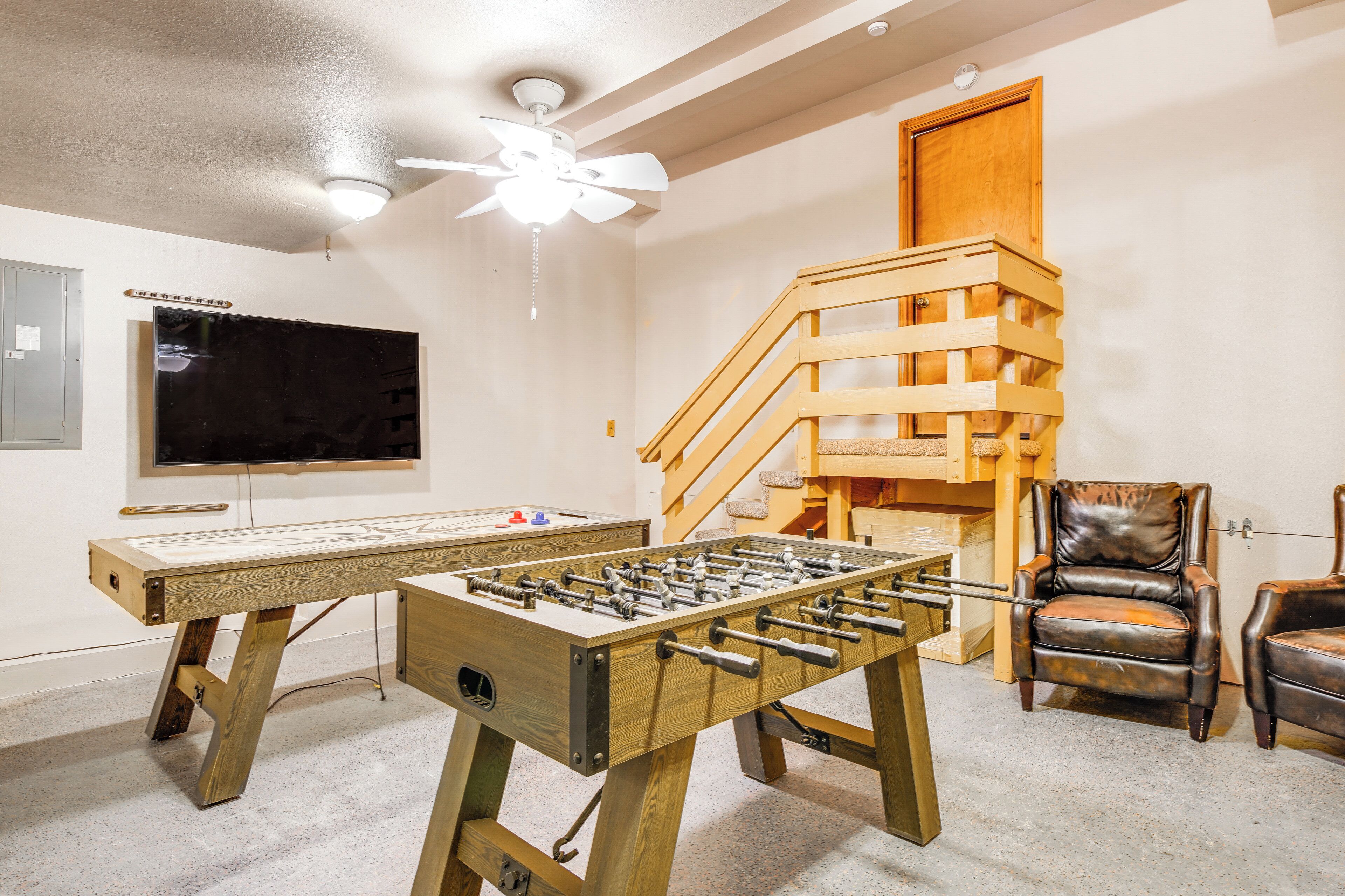 A room with a foosball table, a television, a staircase, and leather chairs.