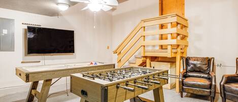 A room with a foosball table, a television, a staircase, and leather chairs.