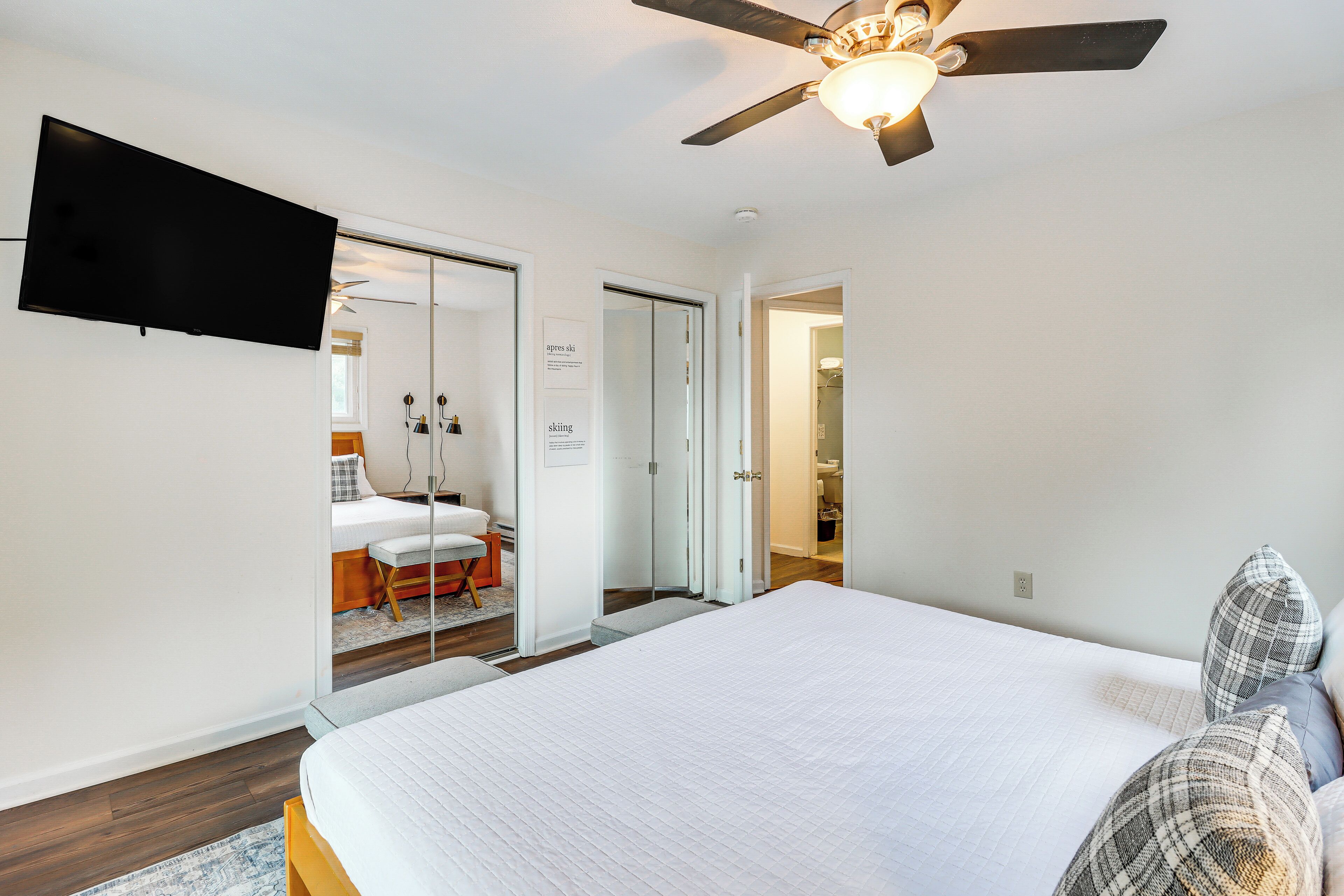 A bedroom with a large bed, a ceiling fan, and a flat-screen TV mounted on the wall.