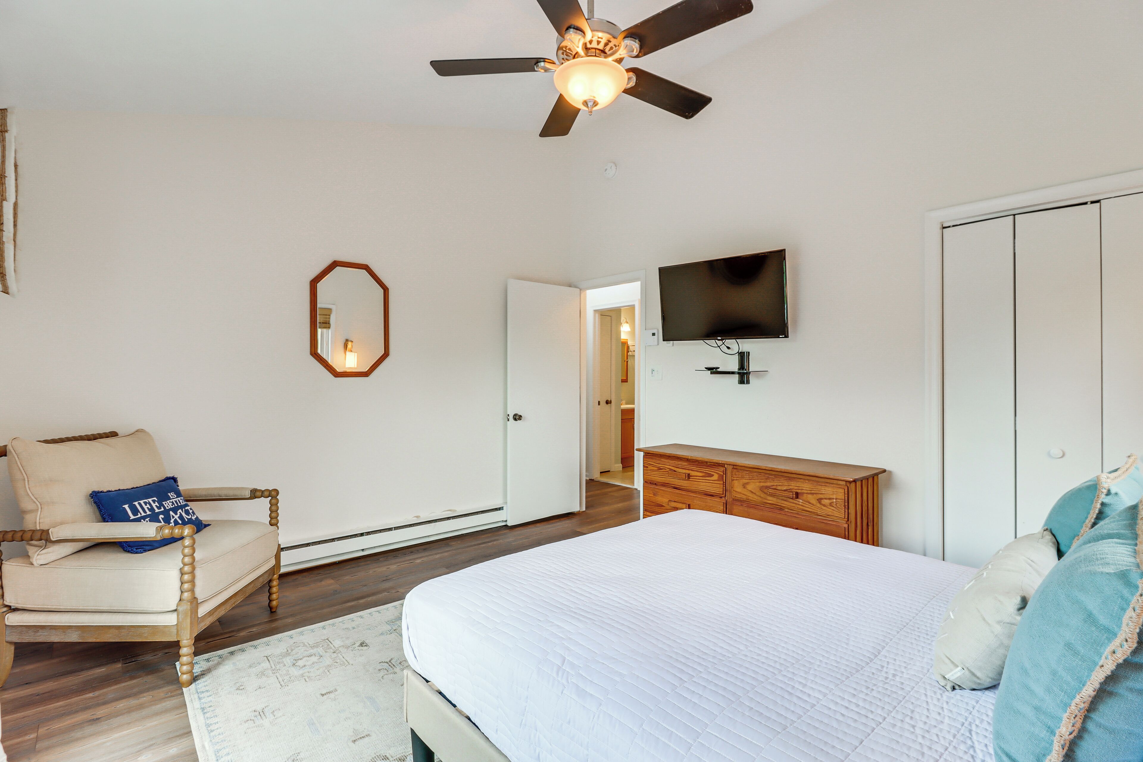 Ein Schlafzimmer mit Bett, Stuhl, Kommode, Fernseher und Deckenventilator.