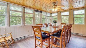 A dining area with a wooden table and chairs, large windows, and a ceiling fan. - Spacious Family Retreat: Pocono Home w/ Deck (Albrightsville)