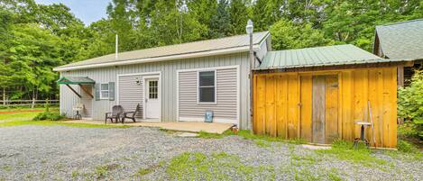 A single-story building with a gravel driveway, a covered patio area with outdoor seating, and a wooden shed.
