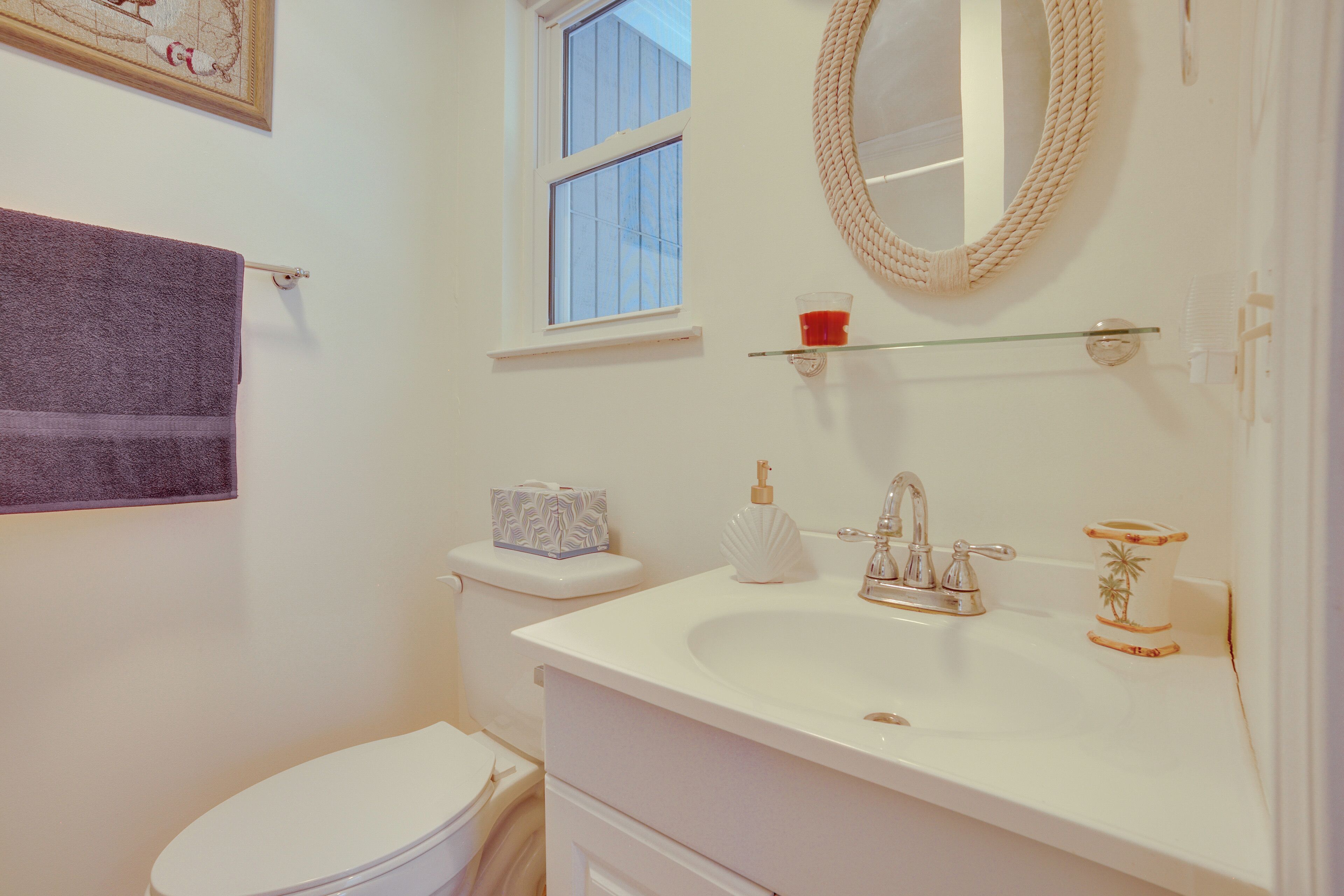 A bathroom with a white sink, a mirror, a window, and a towel rack.