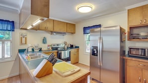 Una cocina moderna con armarios de madera, electrodomésticos de acero inoxidable y una isla central con tabla de cortar y cuchillos.