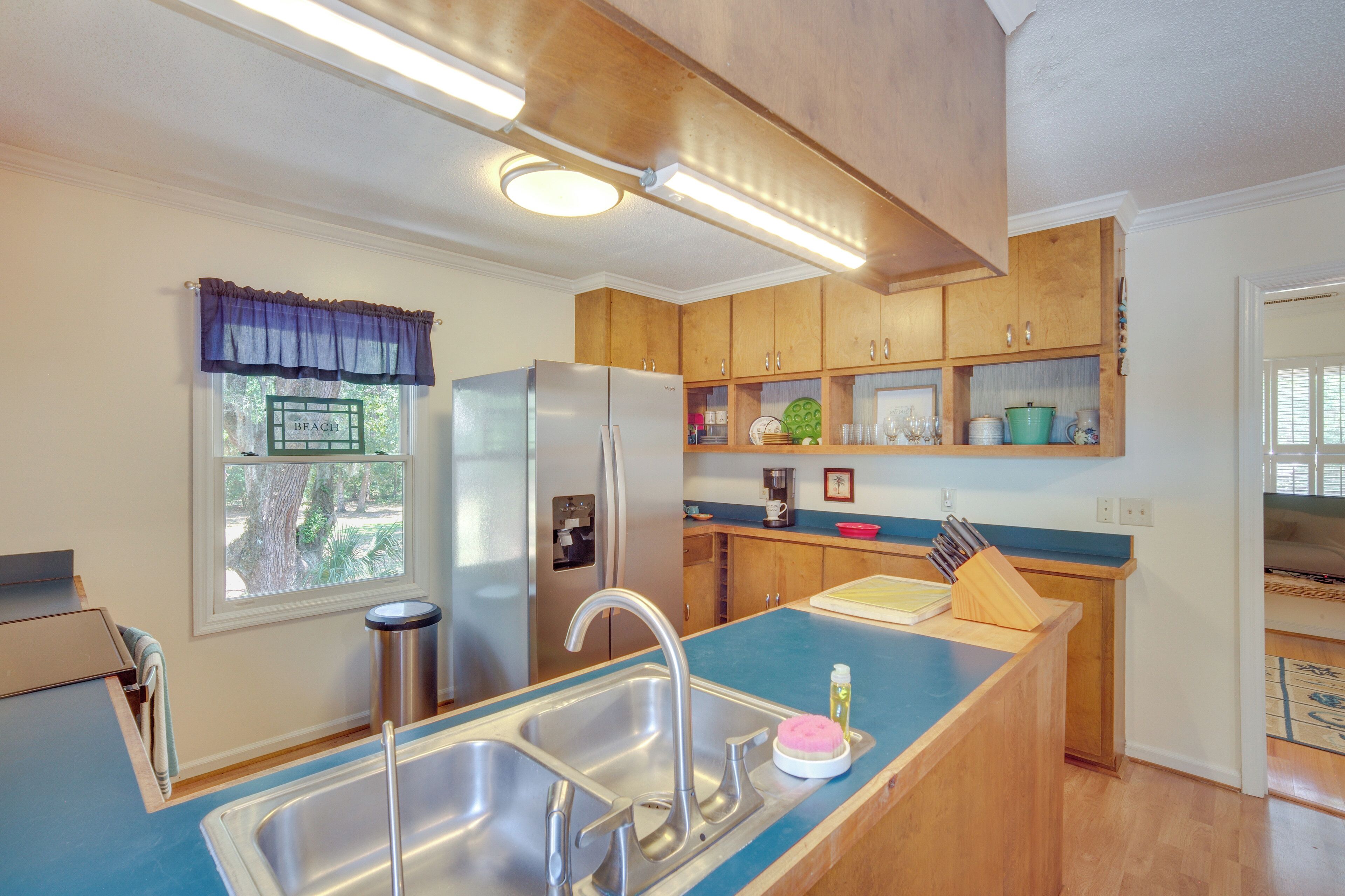 A kitchen with wooden cabinets, a stainless steel refrigerator, a sink, and a window with a view of trees.