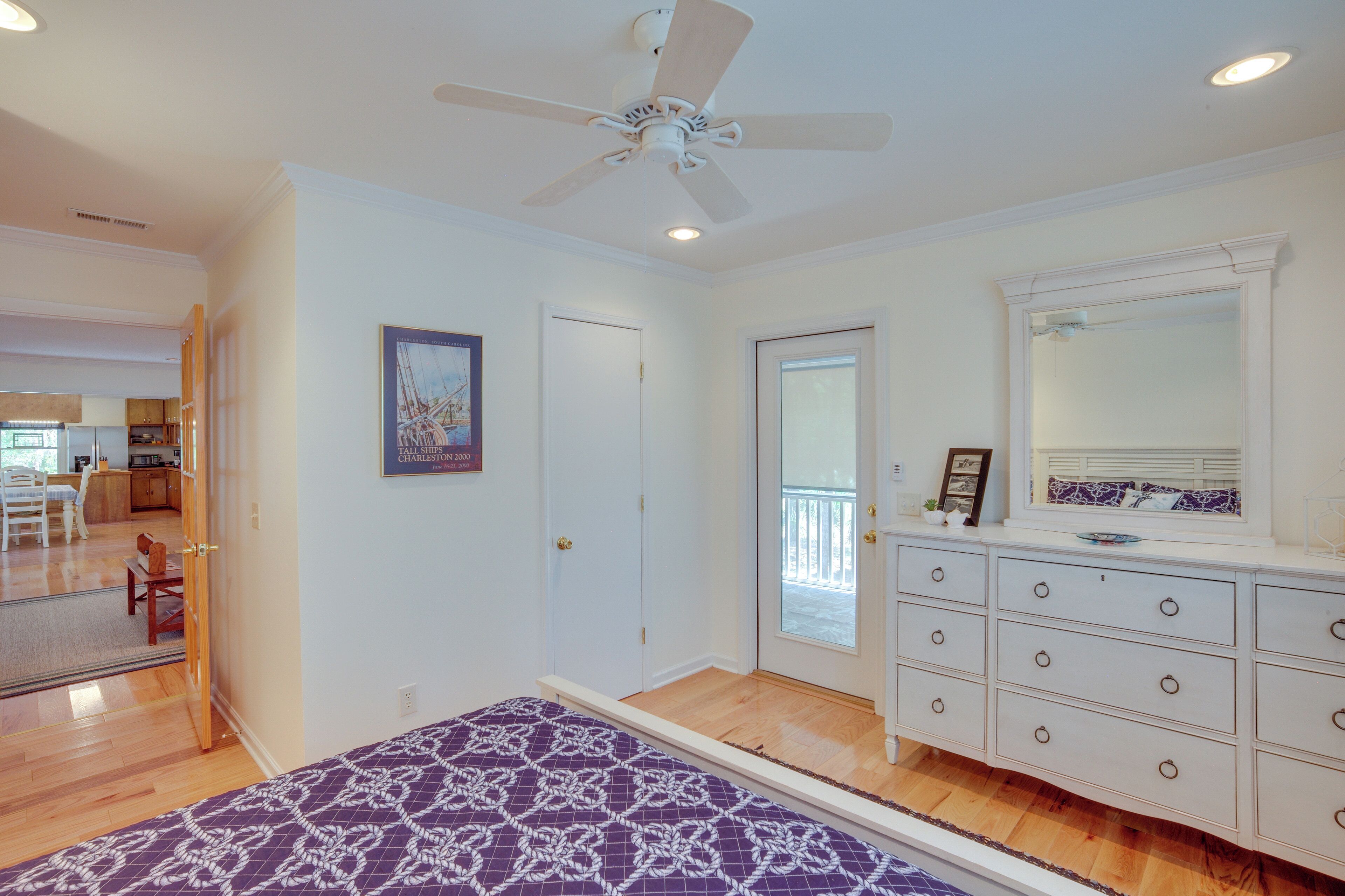 Quarto com cama, penteadeira, ventilador de teto e porta que dá para outro espaço.